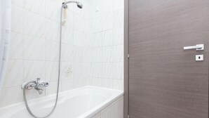 A bathroom with a white bathtub, a shower with a handheld showerhead, and a wooden door. - Apartop (Rome)
