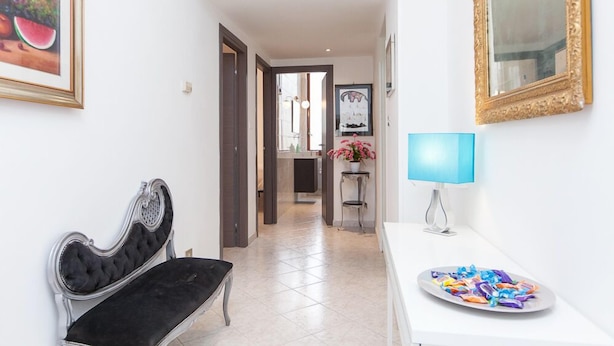 A hallway with a black velvet bench, a white table with a blue lamp, and a plate of colorful candies. - Apartop (Rome)