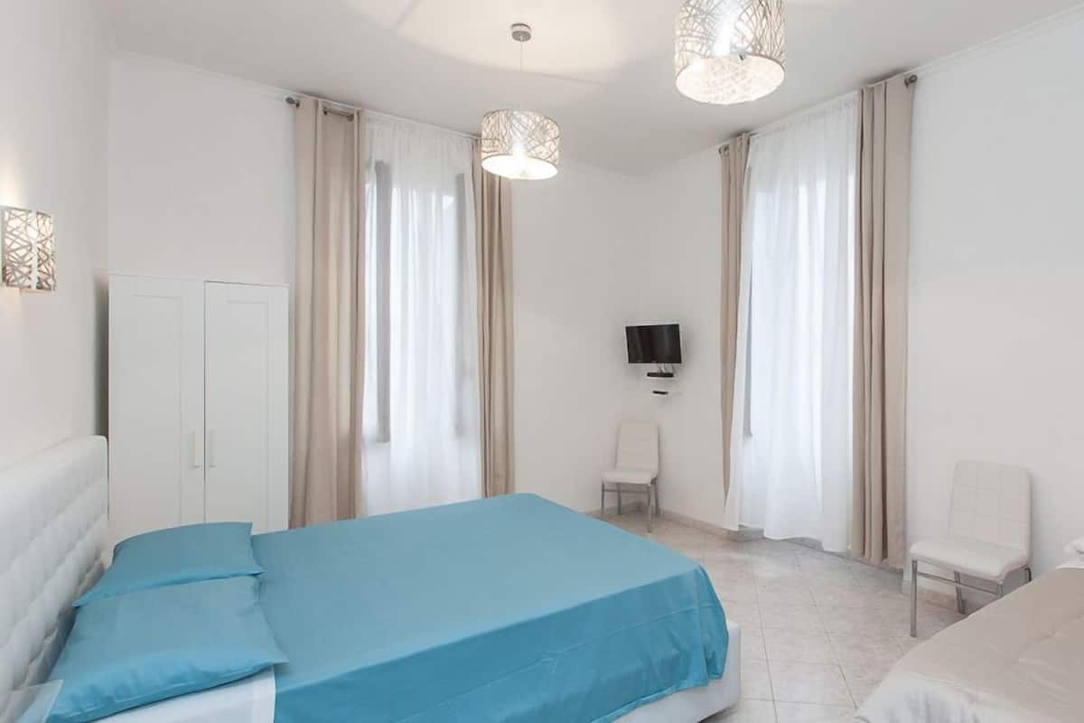 Une chambre d’hôtel avec un lit, une chaise, une télévision et des rideaux.