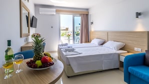 A hotel room with a bed, a blue armchair, a table with a fruit bowl and glasses, and a TV on the wall. - Paul Marie Hotel Apartments (Ayia Napa)