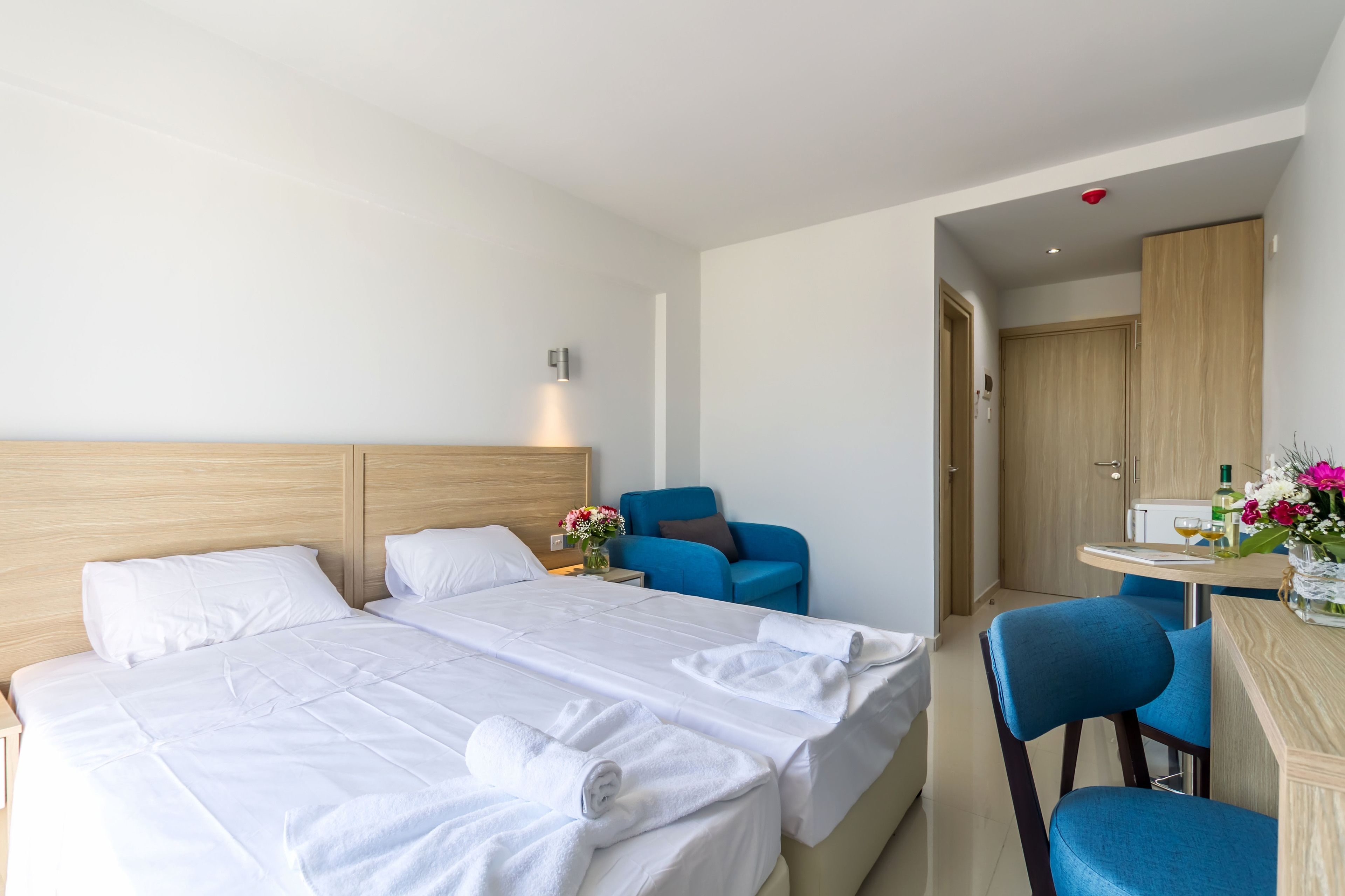 A hotel room with two beds, a desk, a chair, and a small table with a vase of flowers.