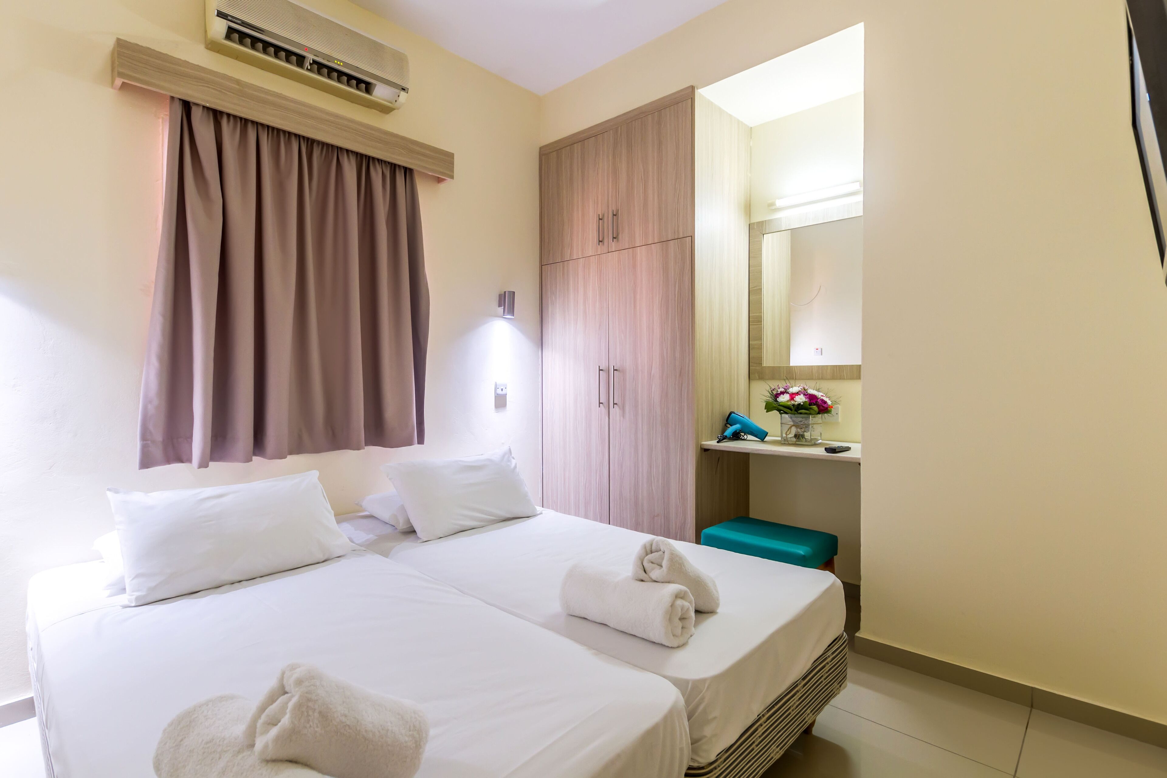 A hotel room with a bed, a wardrobe, a mirror, and a small table with a vase of flowers.