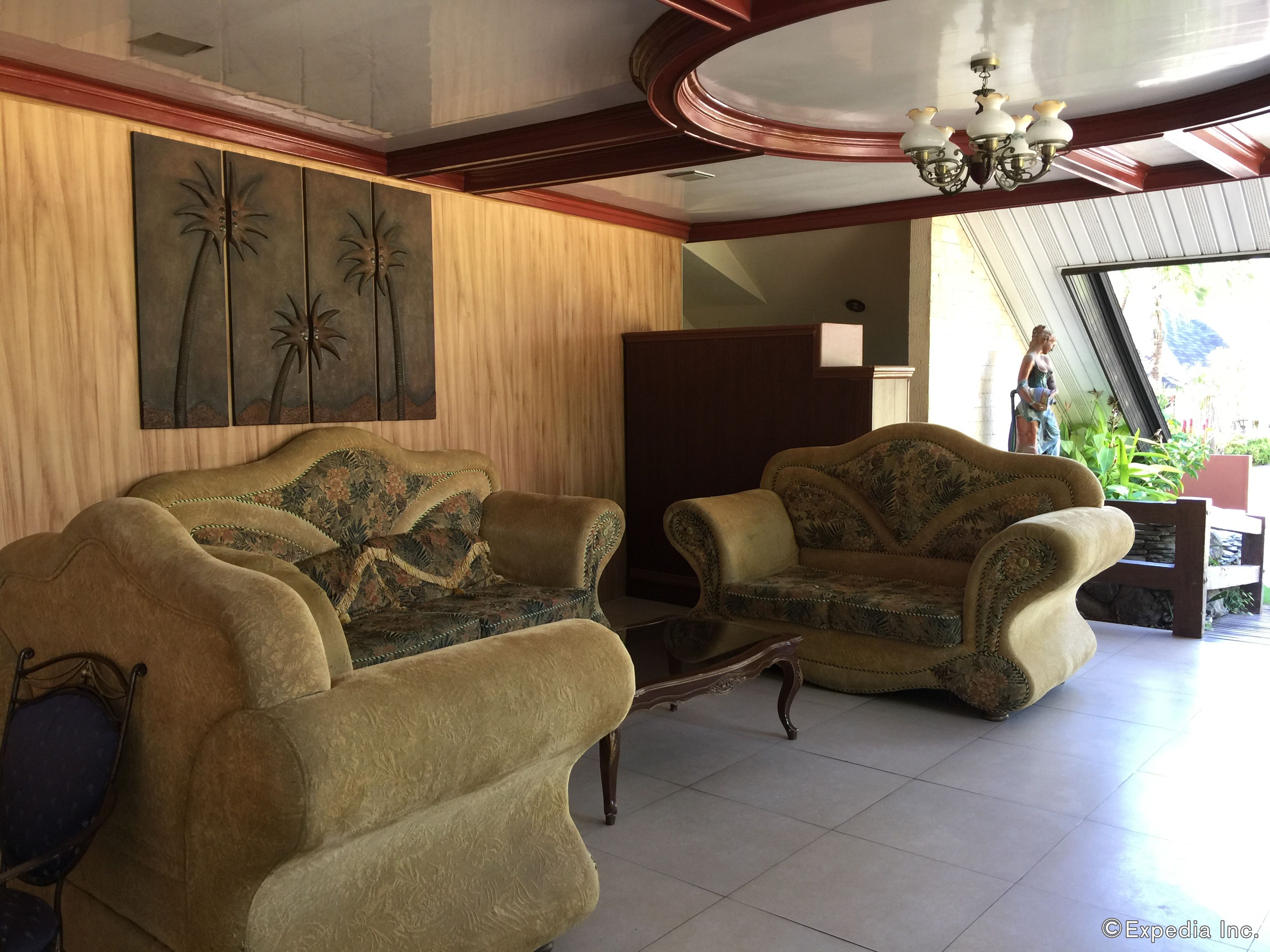 A spacious living area with two sofas and a coffee table, a wooden panel wall with artwork, and a view of a garden through a large window.