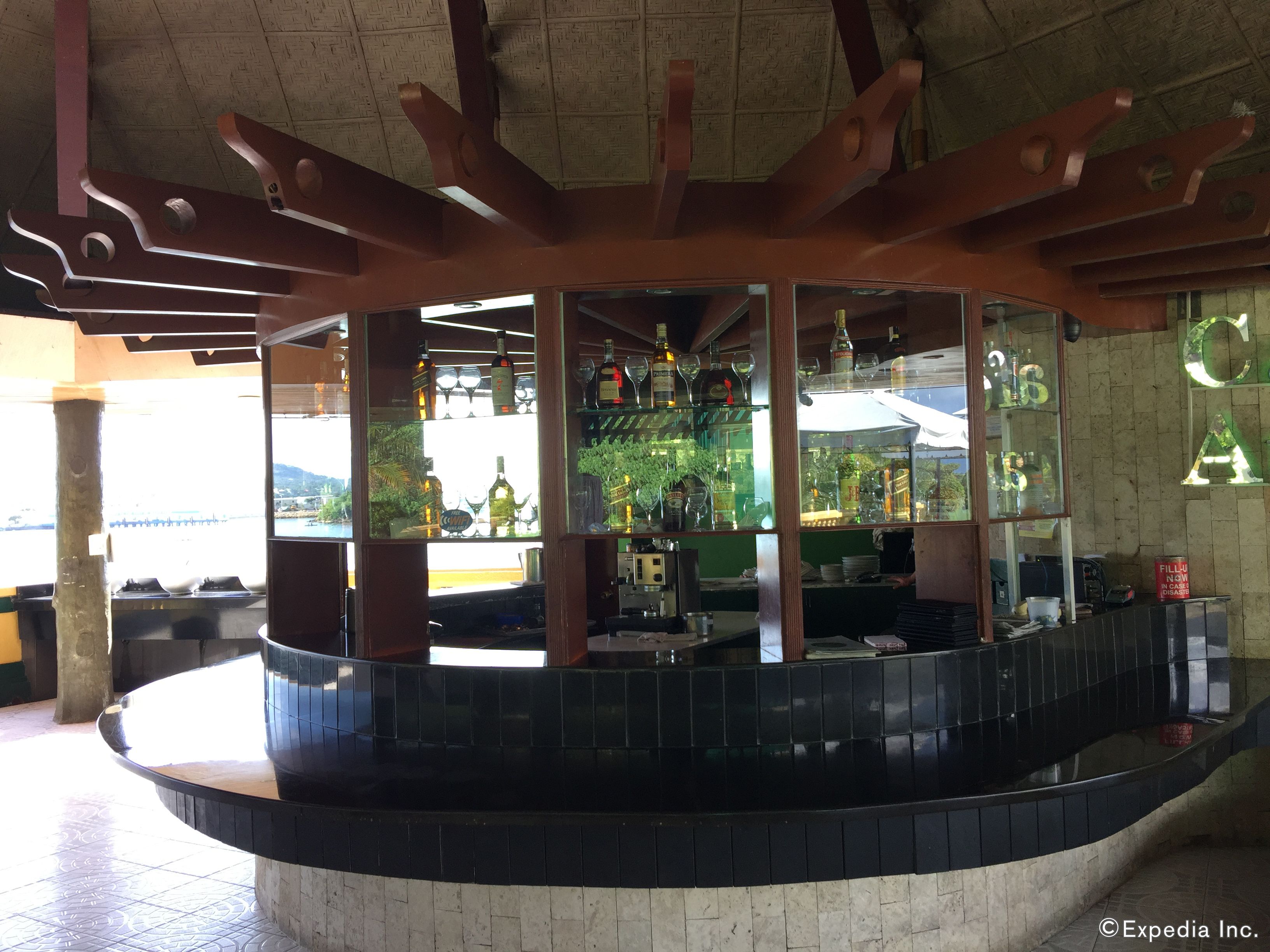 A bar area with a curved counter, shelves with bottles, and a view through the windows.