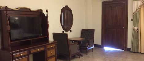 A room with a large wooden TV stand, a small round table, a chair, and a mirror on the wall.