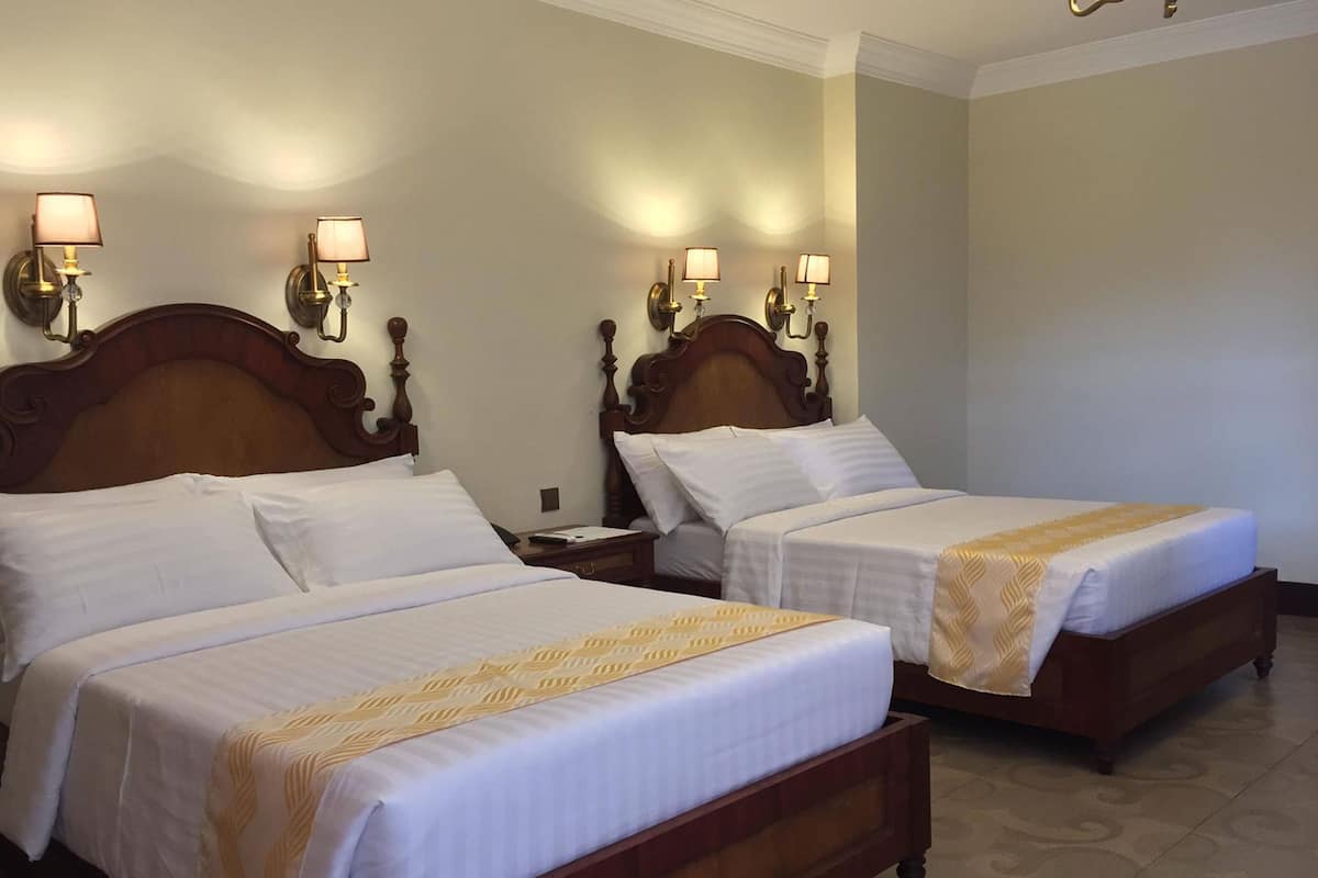 Two double beds with wooden headboards and white bedding, flanked by nightstands with lamps.