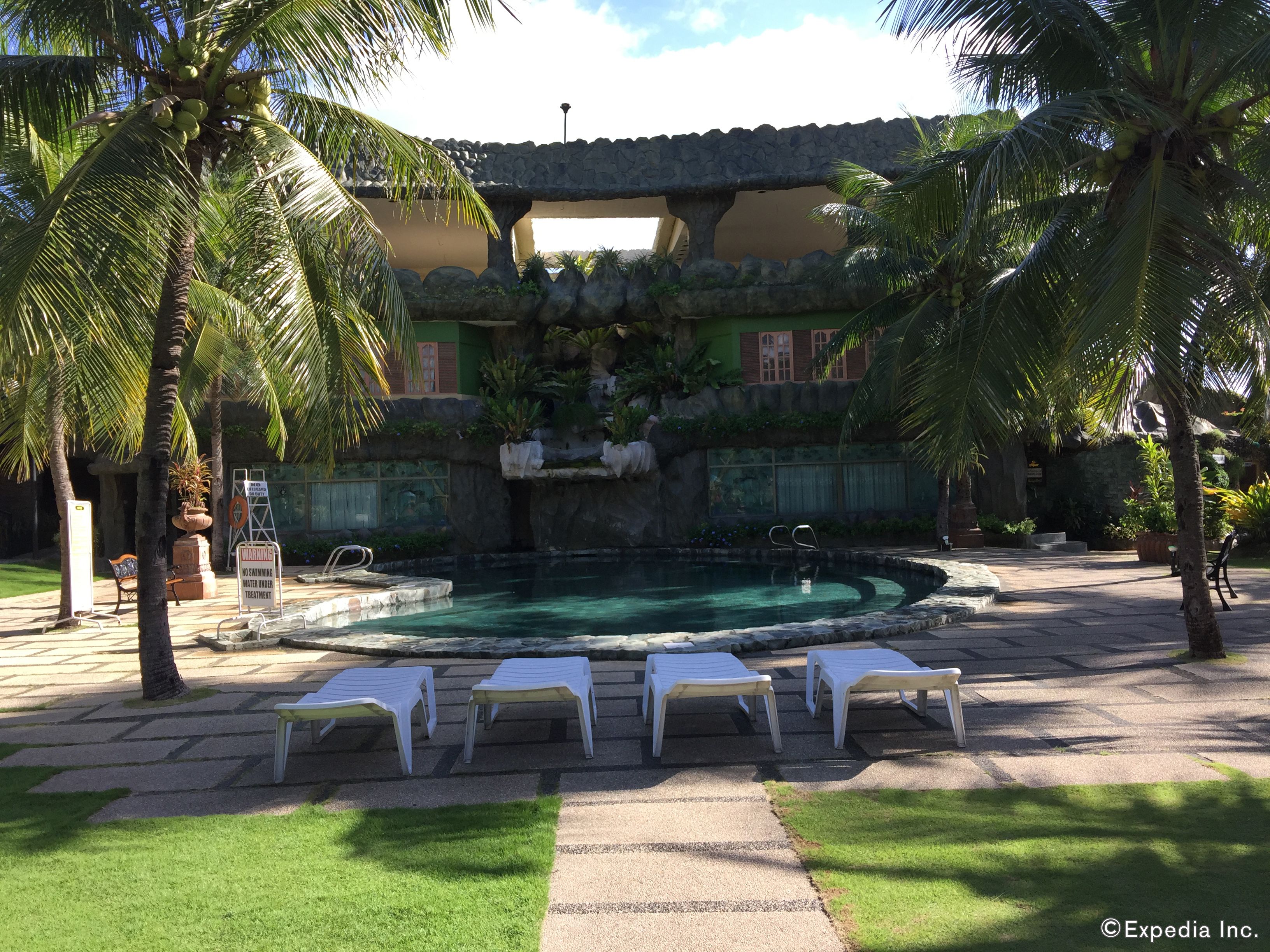 A pool area with lounge chairs, a no swimming warning sign, and a stone structure with plants.