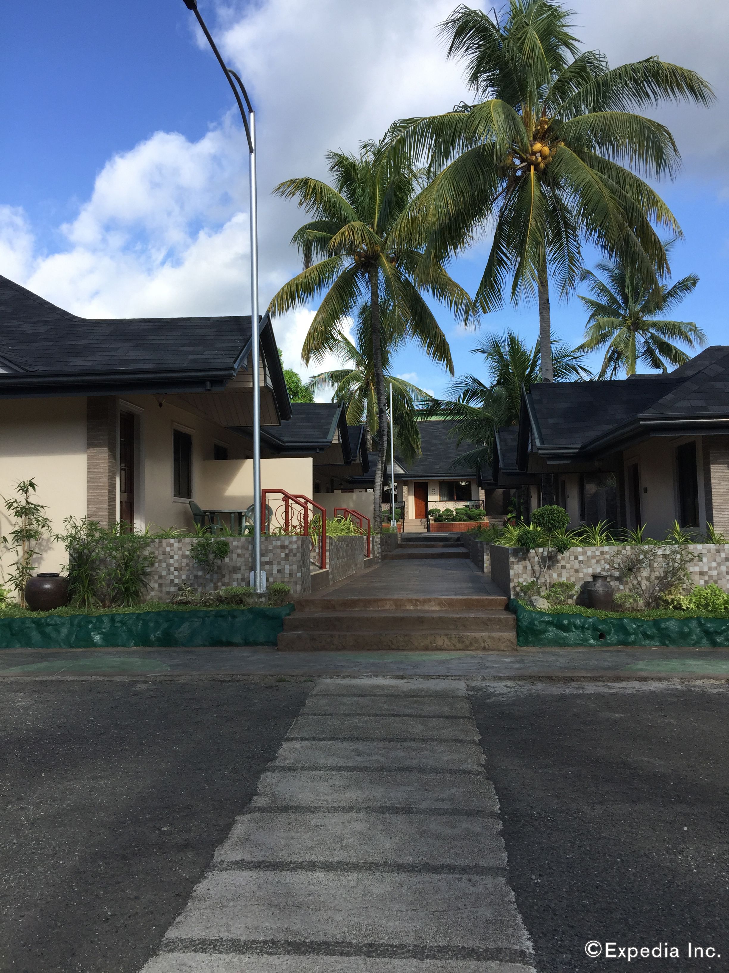 A residential street with houses, palm trees, and a clear sky.