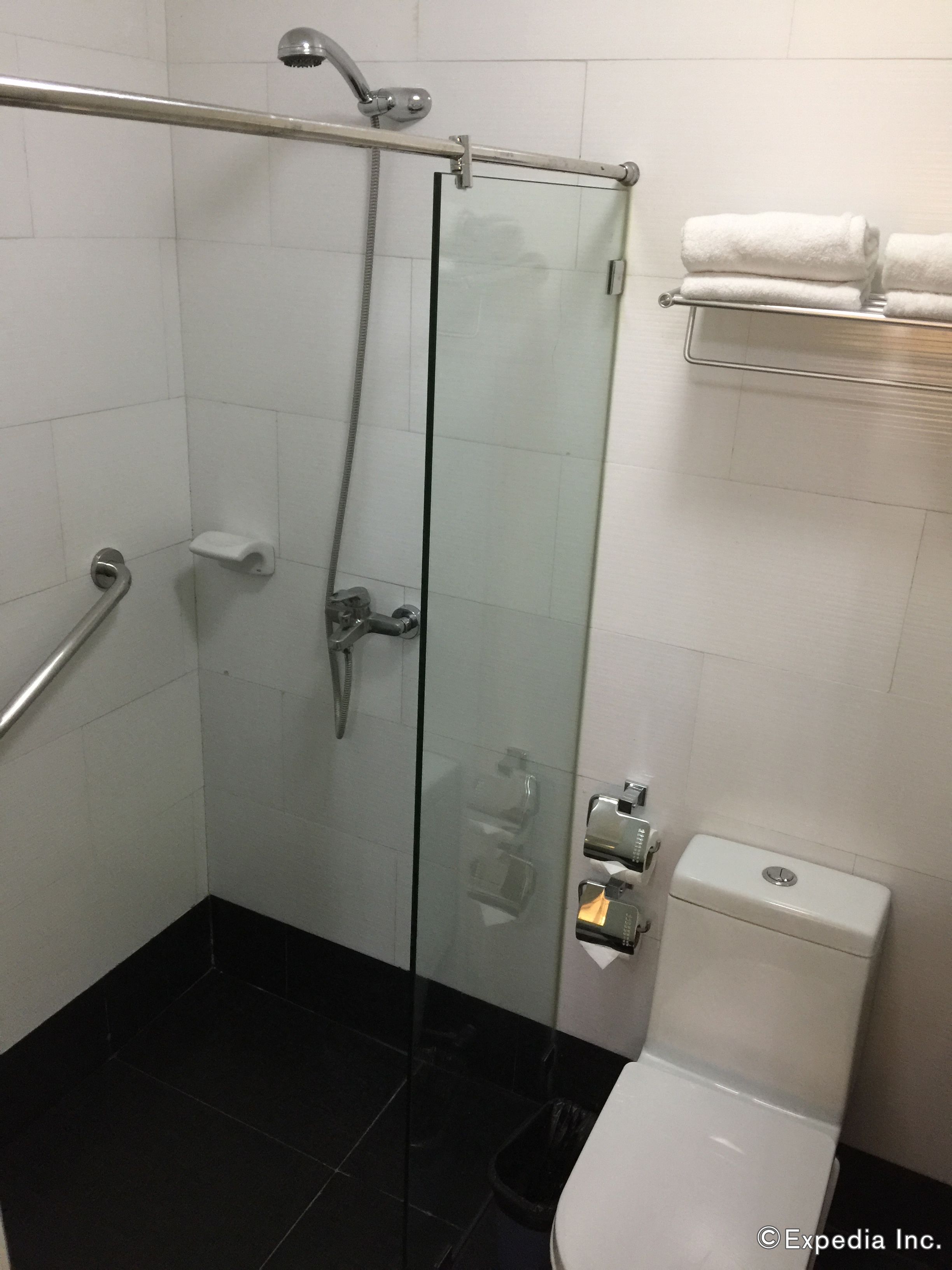 Un baño con mampara de vidrio, inodoro blanco, toallero y barra de apoyo.