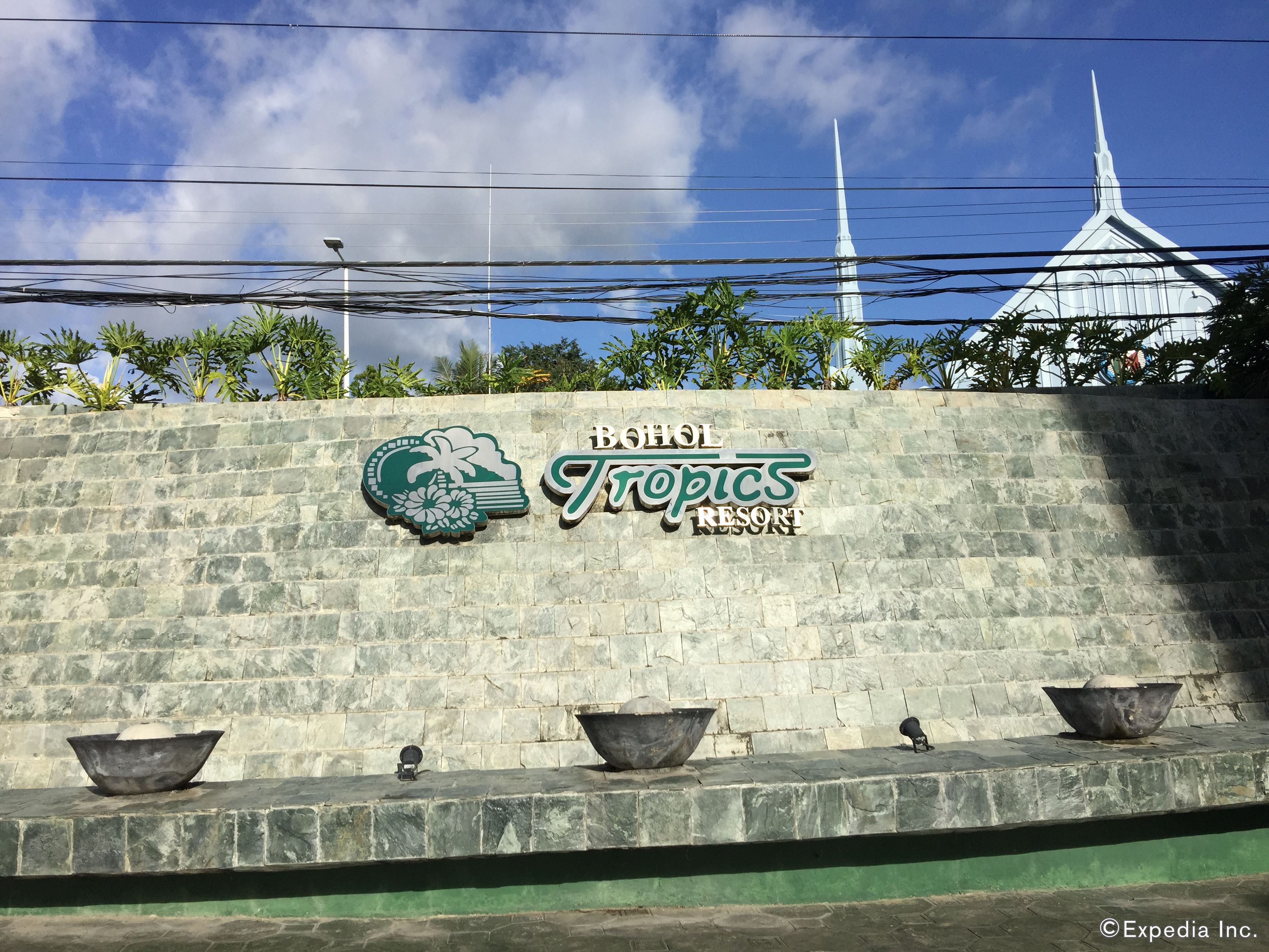 A sign for 'Bohol Tropics Resort' with a tropical design, a stone wall, and three large bowls on the ledge.