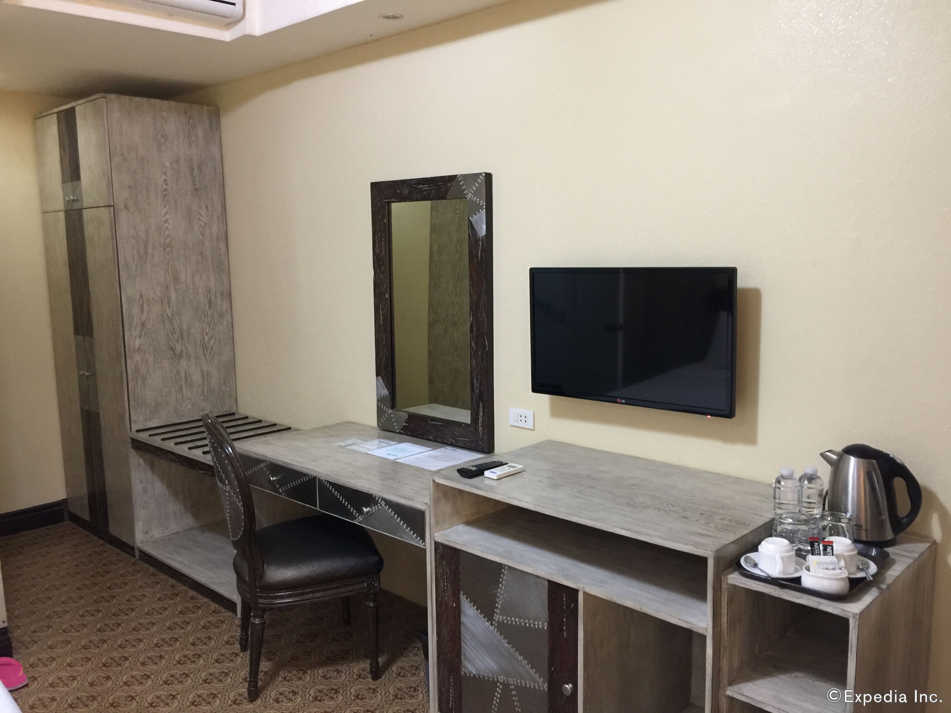 A hotel room with a desk, a chair, a flat-screen TV, a coffee maker, and a tray with cups and a spoon.