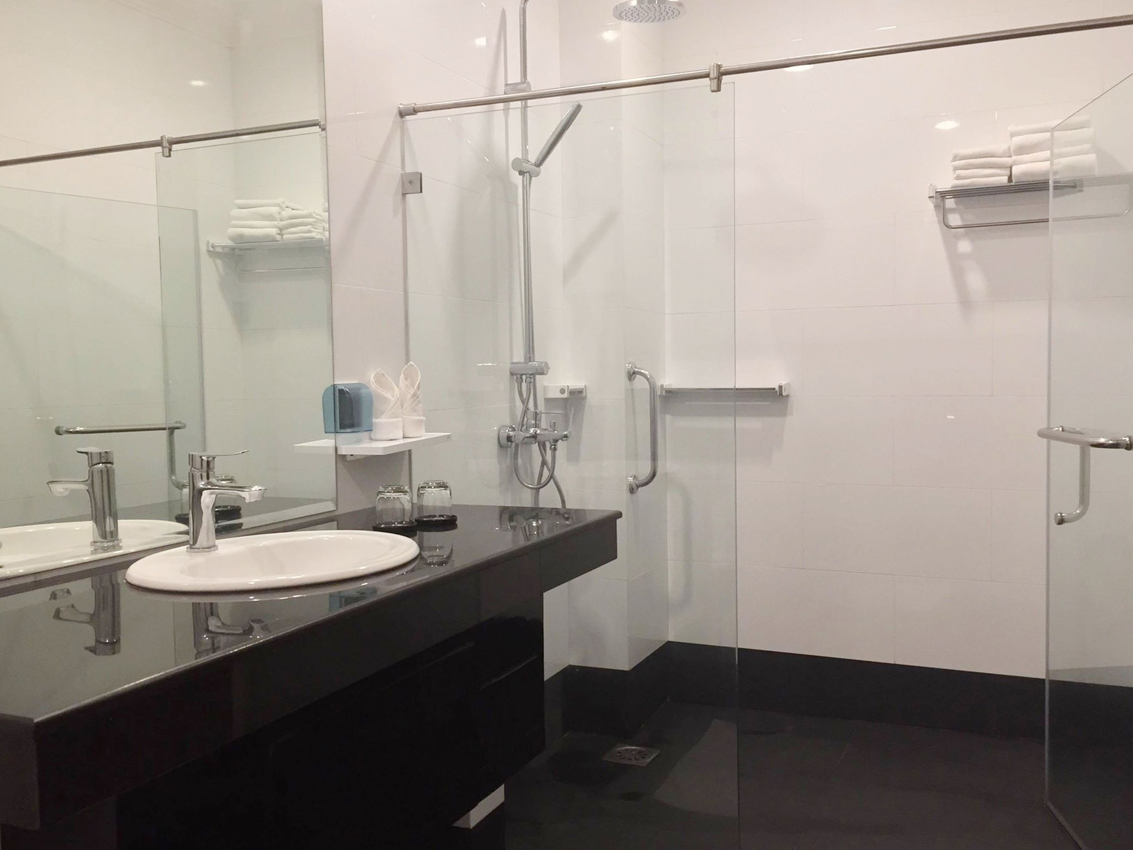 Un baño moderno con cabina de ducha de vidrio, encimera negra y lavabo blanco.