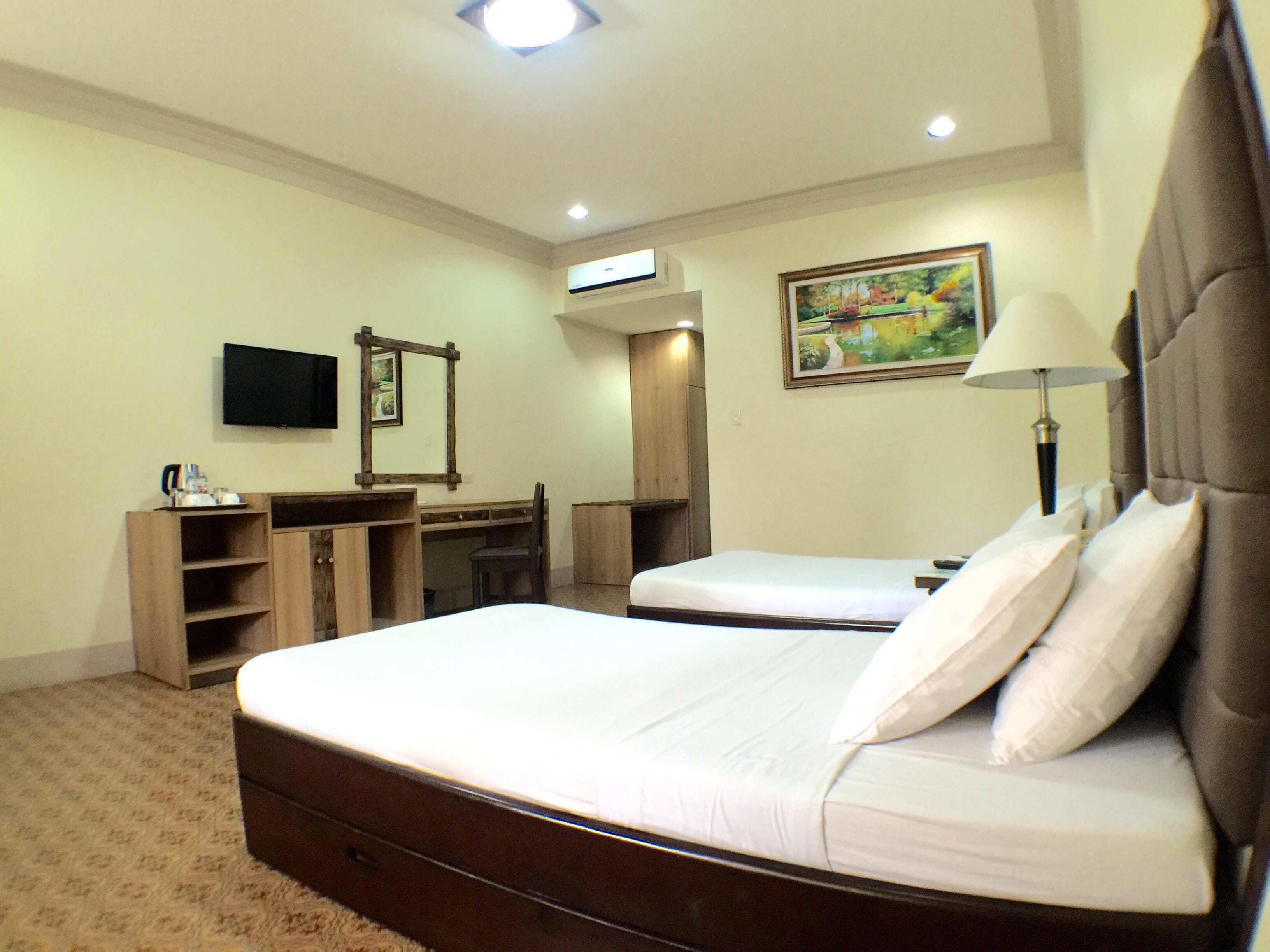 A hotel room with a large bed, a desk, a chair, a television, and a painting on the wall.