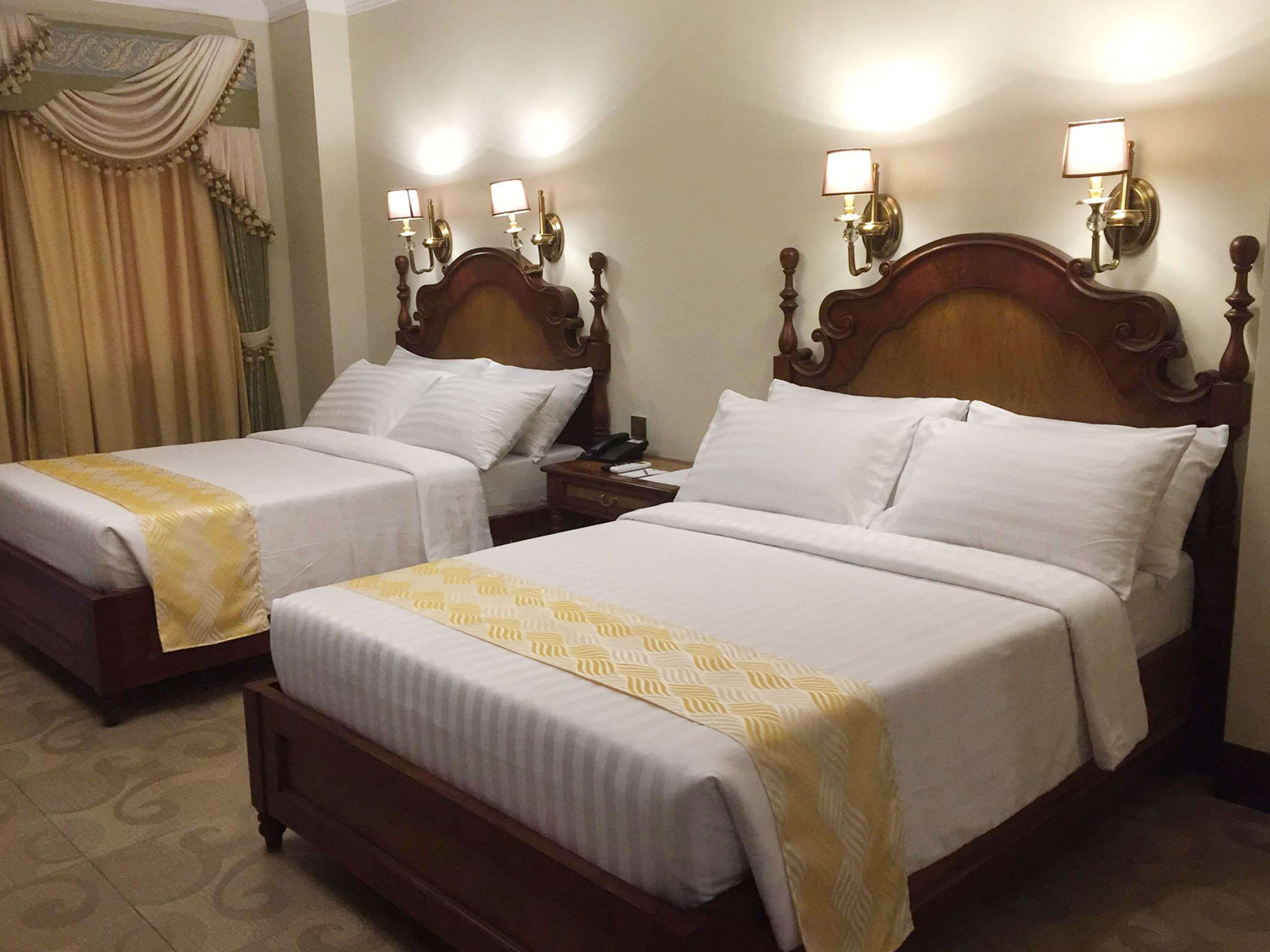 Two double beds with wooden headboards, white linens, and a yellow patterned throw.