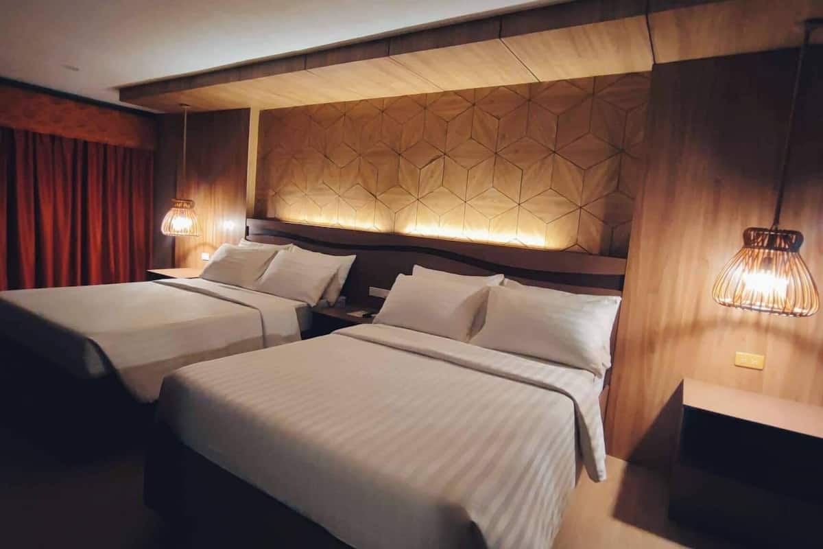 A hotel room with two beds, a geometric patterned headboard, and bedside lamps.