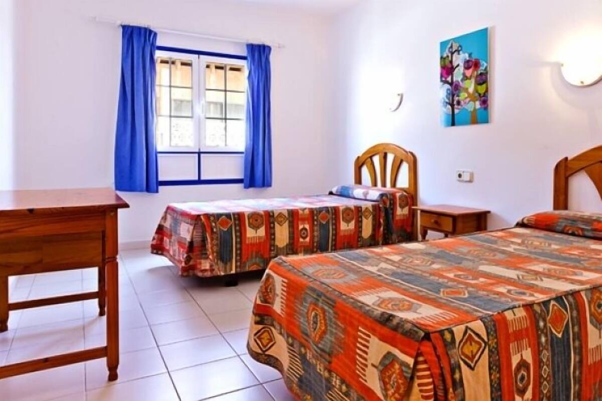 Un dormitorio con dos camas, un escritorio de madera y una ventana con cortinas azules.