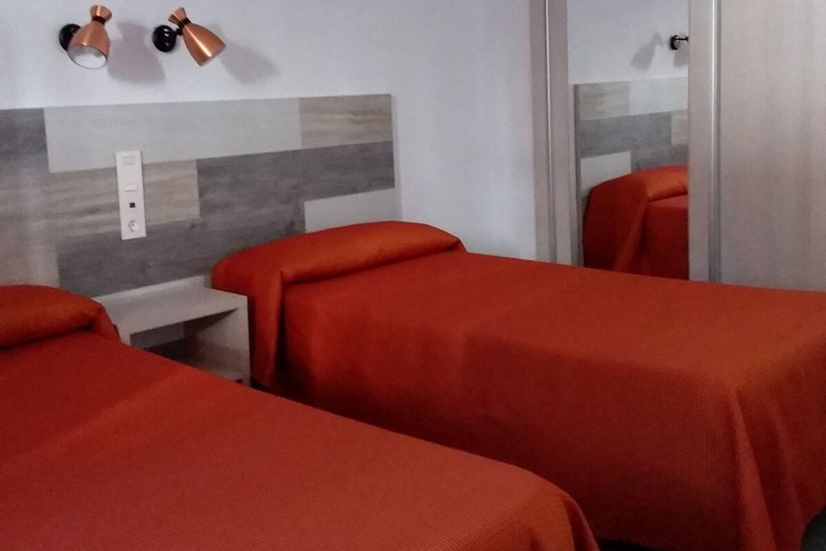Habitación de hotel con dos camas individuales, cabecero de madera, un espejo y una puerta con picaporte.