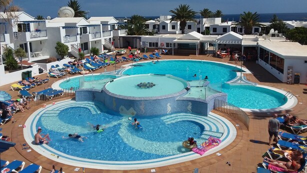 A large outdoor swimming pool surrounded by lounge chairs and sunbeds, with a clear view of the ocean in the background. - Atlantis Las Lomas (Tías)