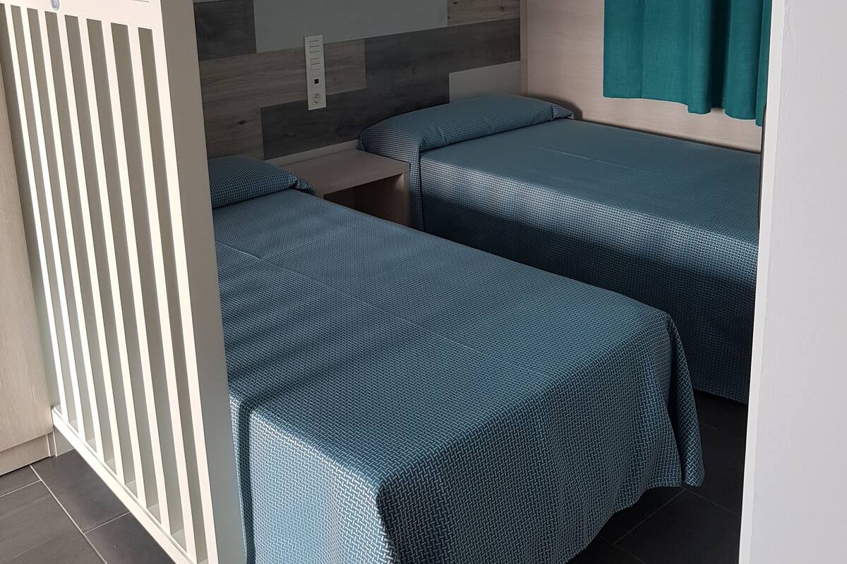 Una habitación con dos camas individuales, una lámpara de pared y una cortina.