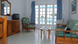A living room with a wooden cabinet, a television, a sofa, a chair, and a table. - Atlantis Las Lomas (Tías)