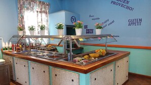 A buffet area with a variety of food items, a wall with motivational phrases, and a window with patterned curtains. - Atlantis Las Lomas (Tías)