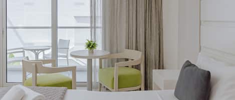 Une chambre d’hôtel avec un lit, une table ronde, deux chaises, une petite table avec une plante et un balcon avec vue.