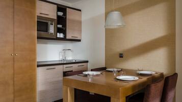 A compact kitchen with a microwave, wooden cabinets, and a dining table set for two with chairs.