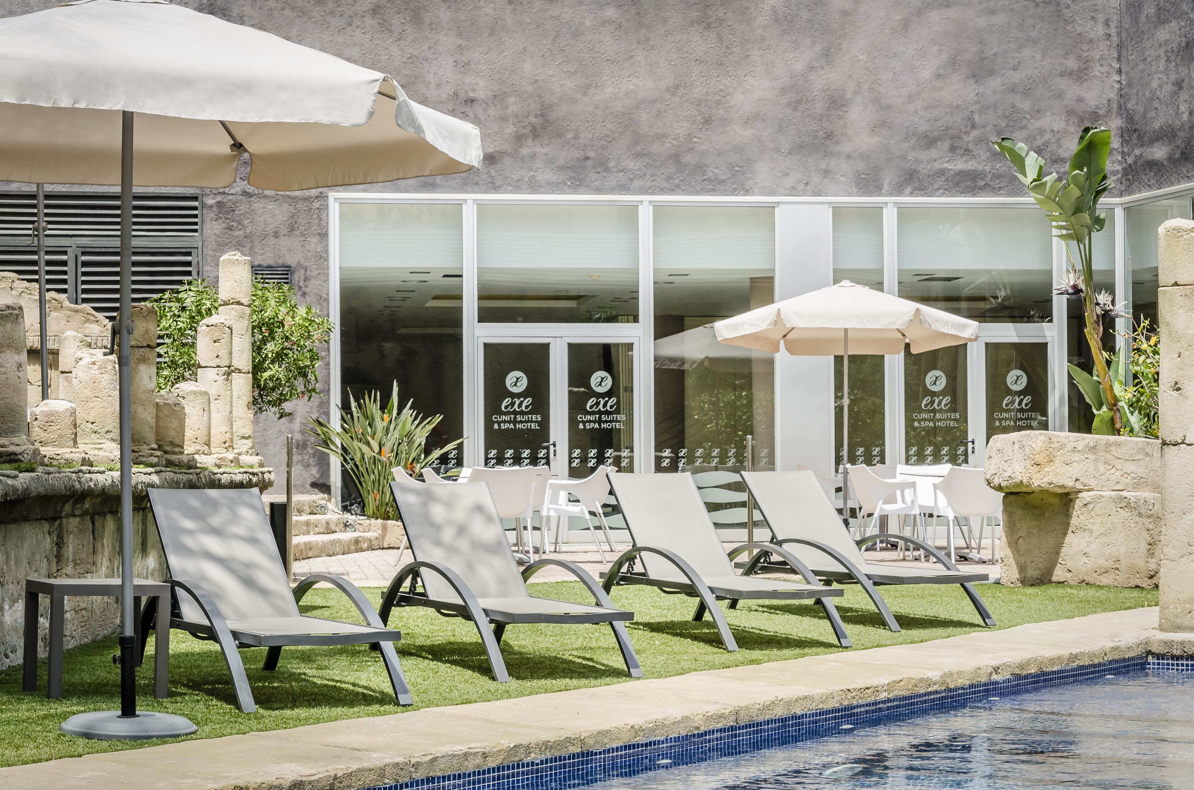 Een zwembadgedeelte met ligbedden en parasols, een stenen fontein en een bord van een wellnesshotel.