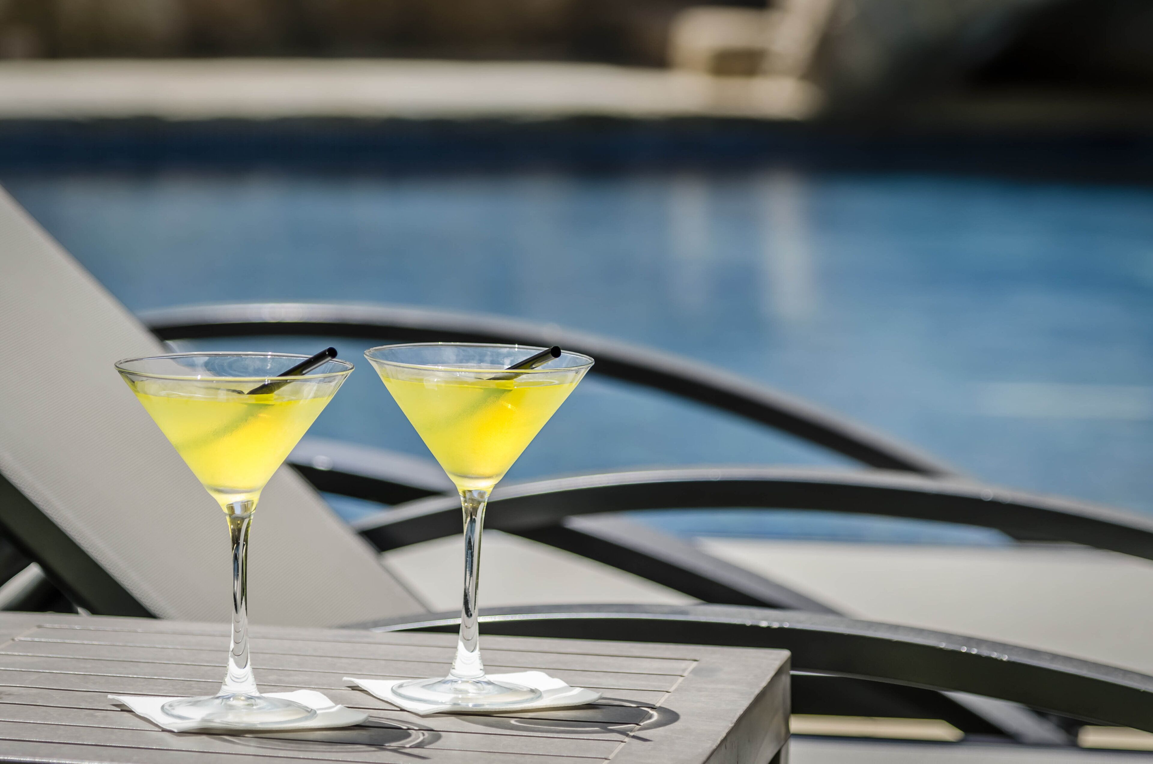 Dues copes de martini amb begudes grogues sobre una taula al costat d'una piscina.