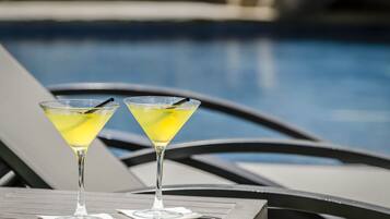 Dues copes de martini amb begudes grogues sobre una taula al costat d'una piscina.