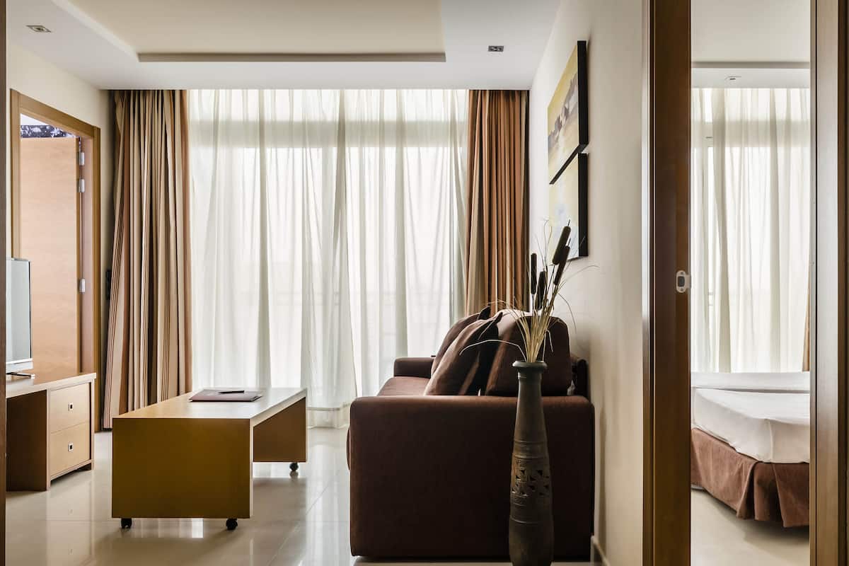A modern hotel room with a sofa, a desk, a vase with plants, and a bed.