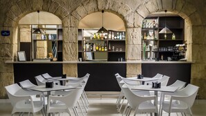 Een bar met witte stoelen en planken vol flessen.