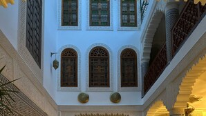 Un patio interior con piscina, paredes ornamentadas y zona de estar con cojines.