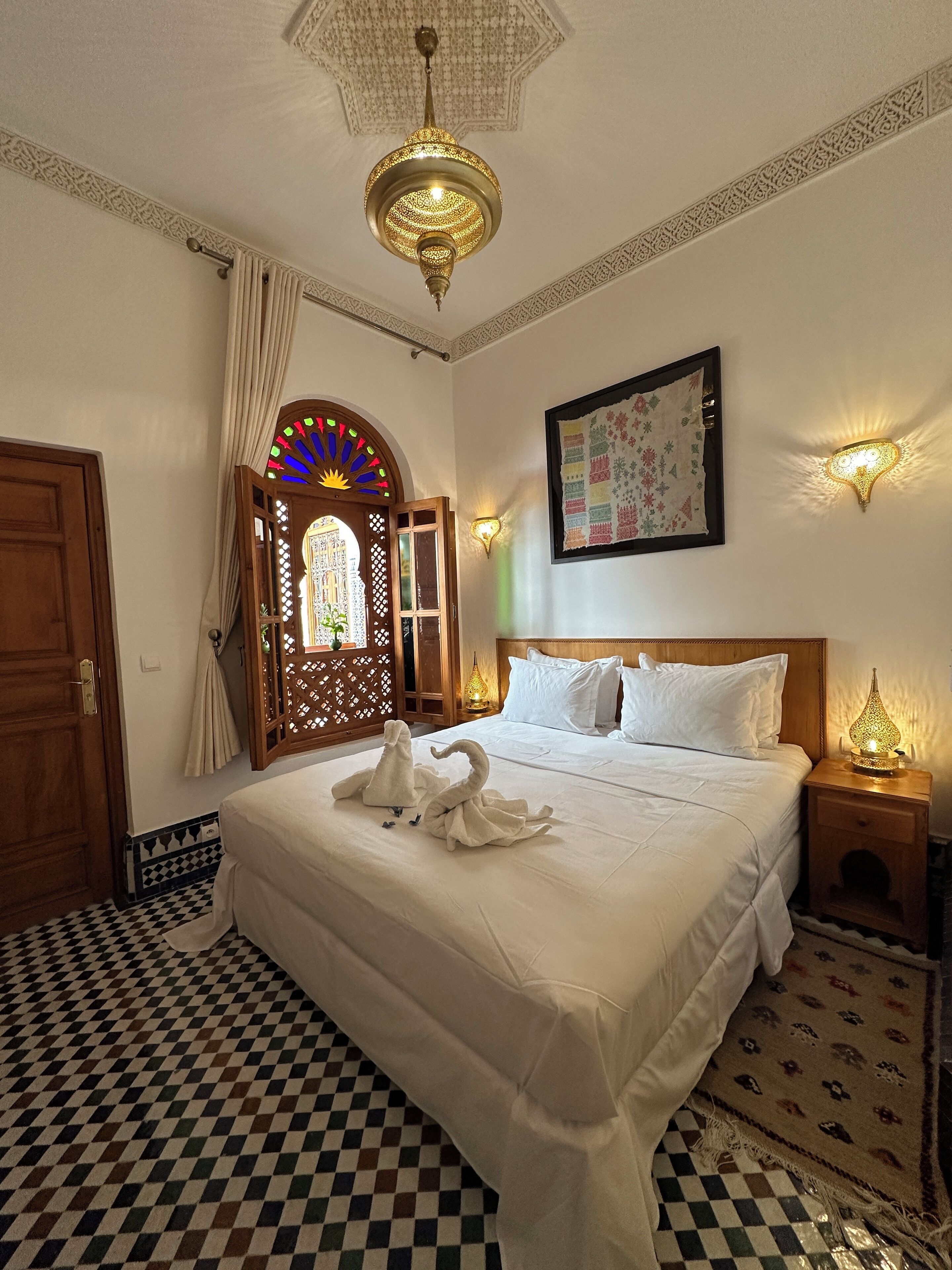 Une chambre d’hôtel avec un grand lit, un lustre, une arche décorative au mur et un tapis à motifs.
