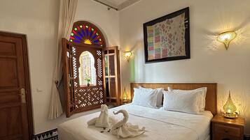 A hotel room with a large bed, a chandelier, a decorative wall arch, and a patterned rug.