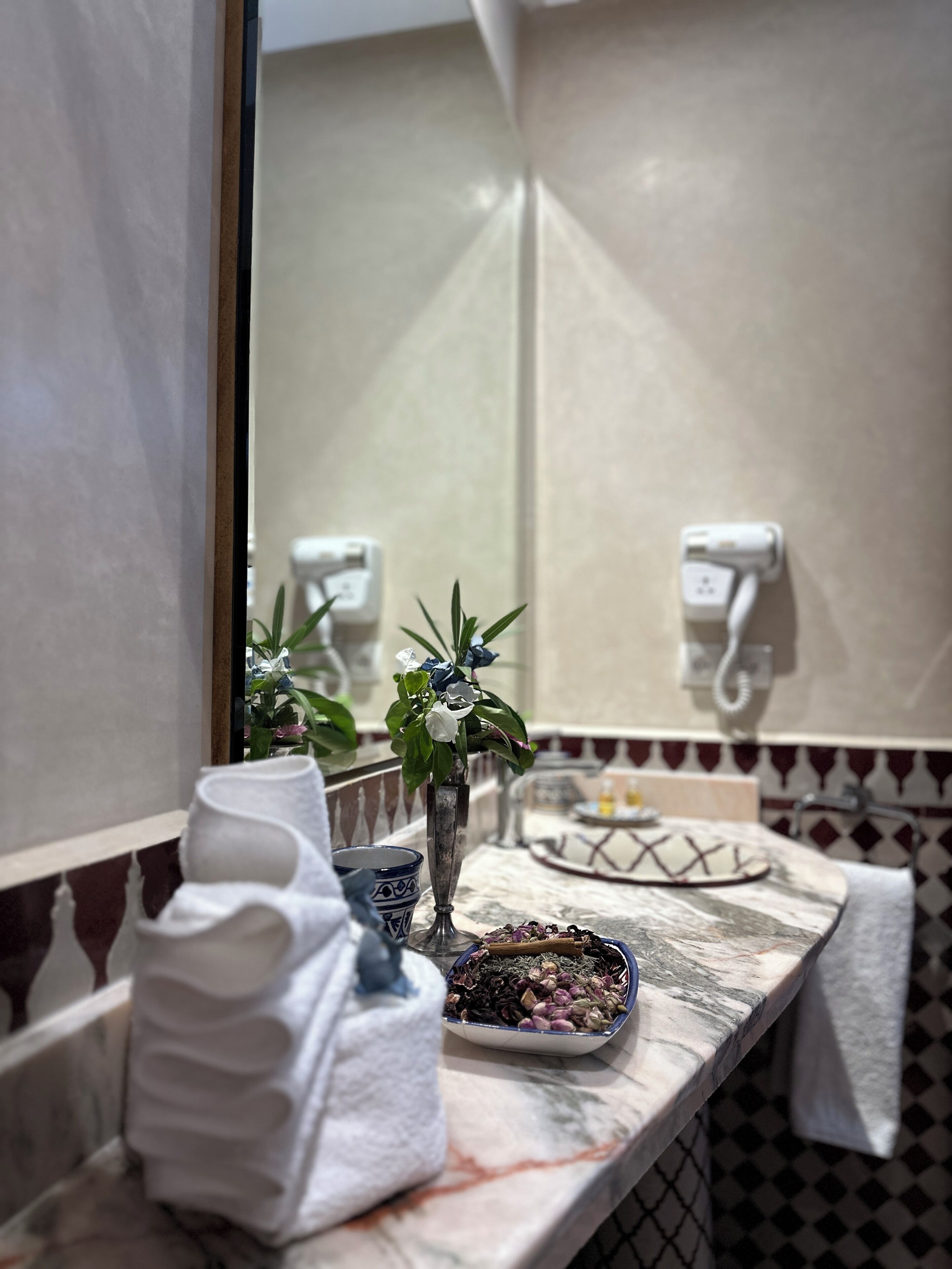 Un baño con encimera de mármol, un jarrón con flores, un cuenco de hierbas y una pila de toallas.