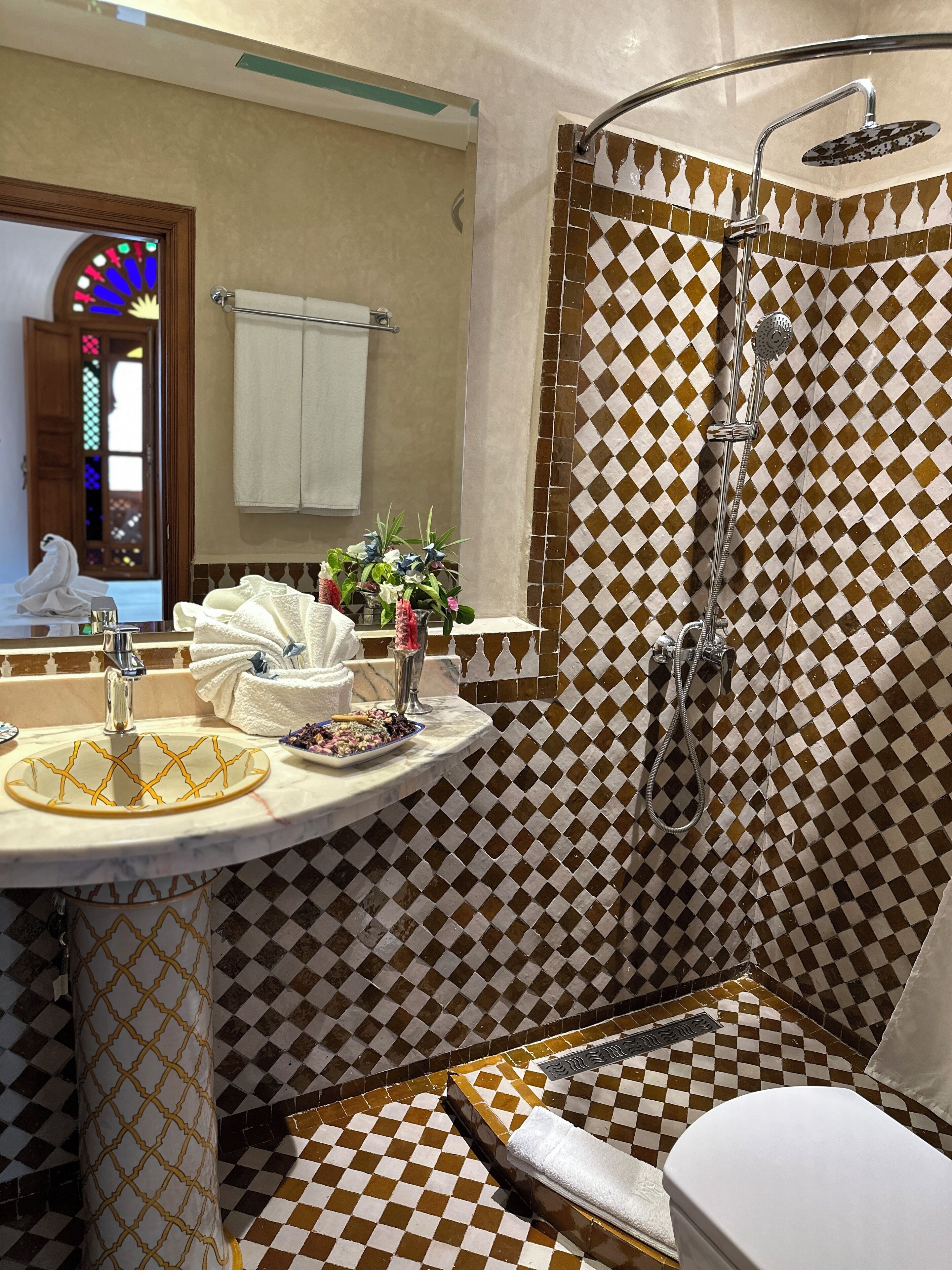 Une salle de bain avec un carrelage à motifs à carreaux, un lavabo doté d’un receveur décoratif, une douche avec un pommeau de douche à main et des toilettes.
