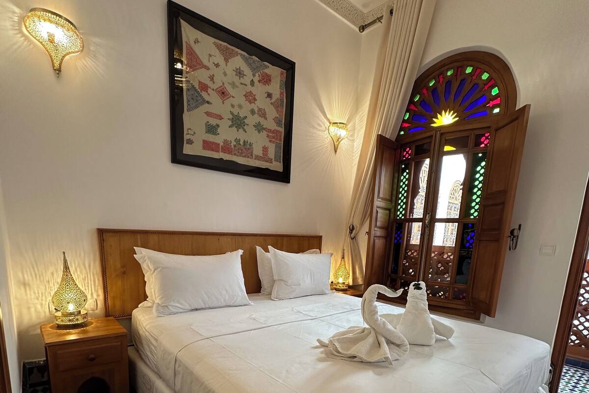 A neatly made bed with white linens, a framed artwork above it, and a patterned rug beside the bed.