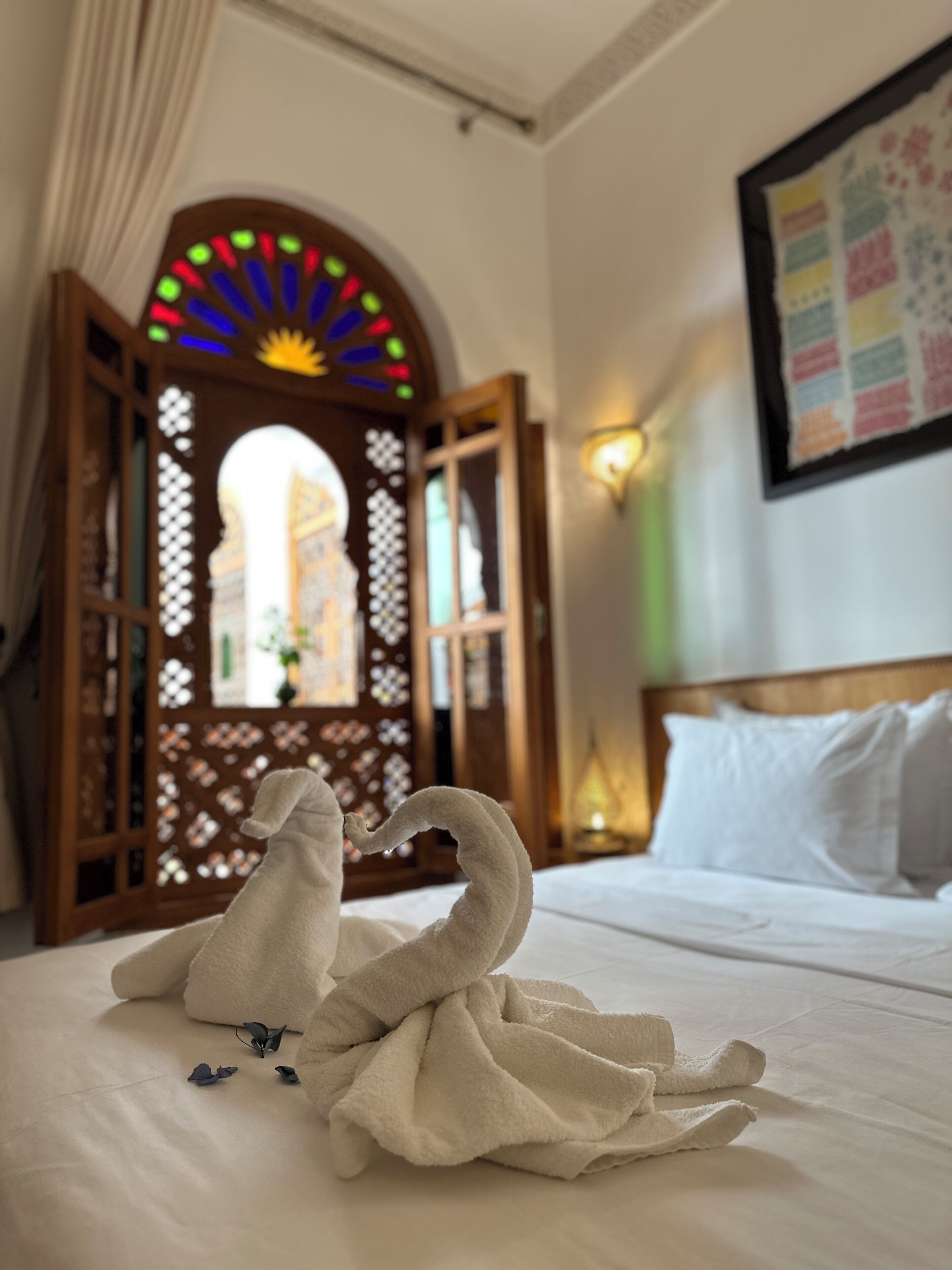 Une chambre d’hôtel avec un lit, un paravent décoratif en bois agrémenté de lumières colorées et un luminaire fixé au mur.
