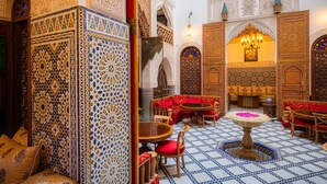 Un interior con detalles intrincados en cerámica, un área de descanso con cojines rojos y una mesa central adornada con un arreglo floral.