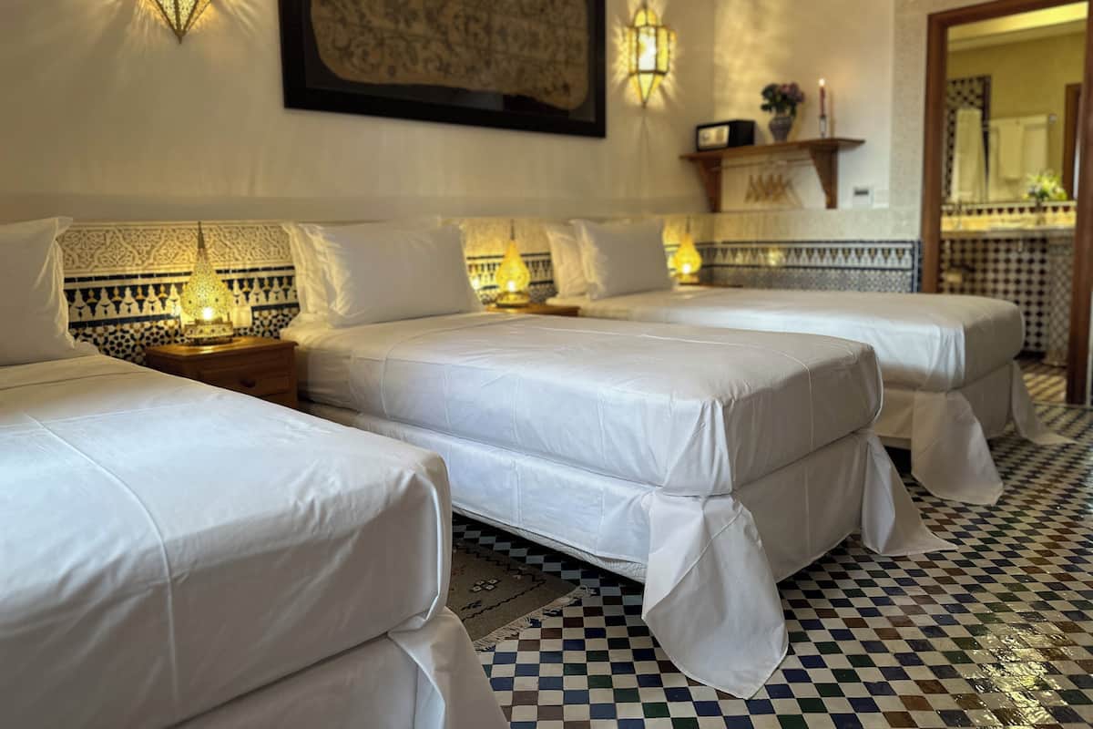 A hotel room with two beds, a checkered floor, wall-mounted lamps, and a large framed artwork.