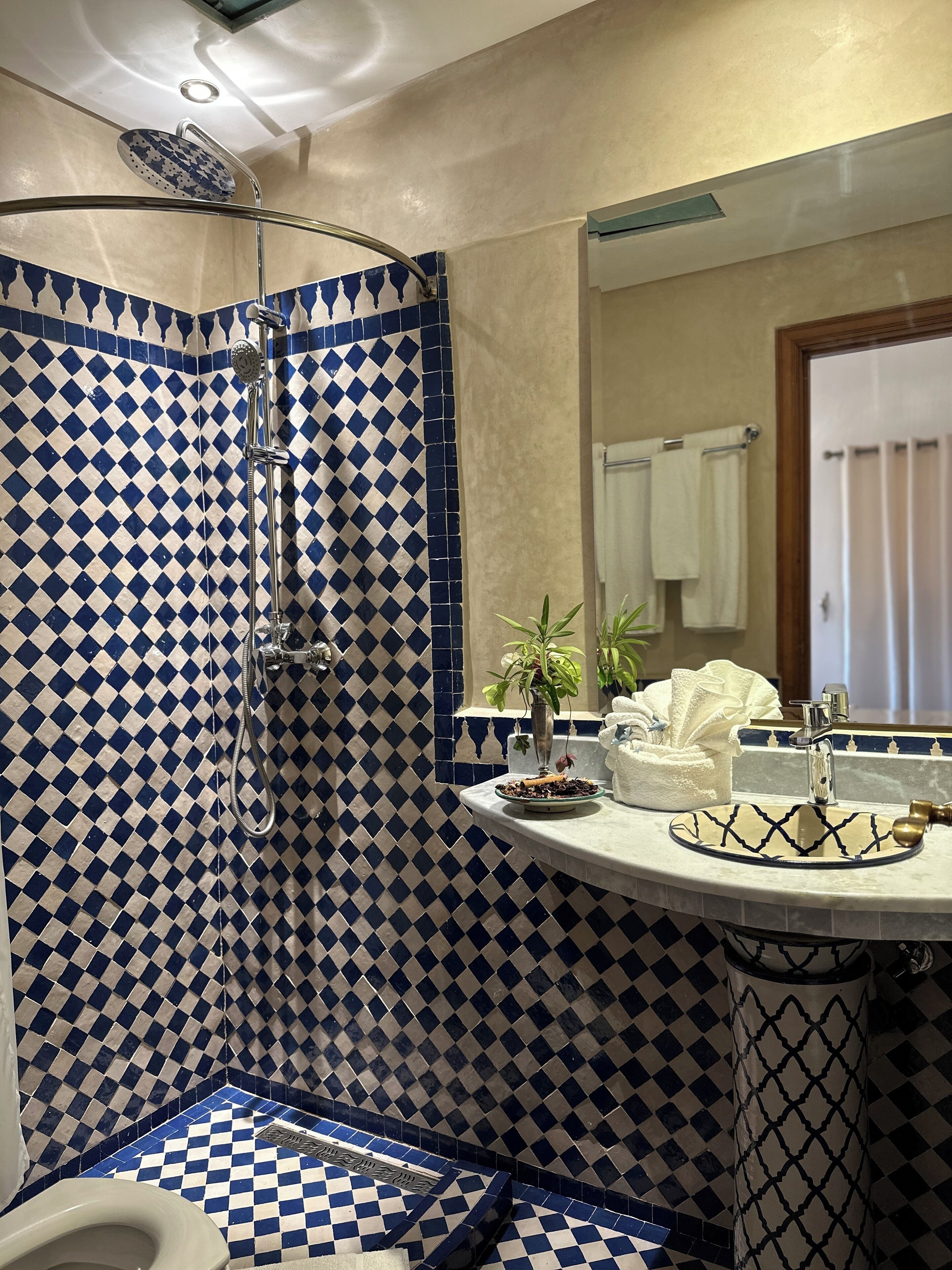 Un baño con suelo de baldosas a cuadros, ducha, lavabo con un cuenco decorativo y espejo.