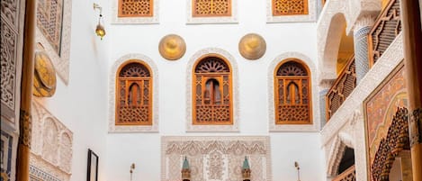 A traditional Moroccan interior with ornate arches, a patterned tile floor, and red upholstered seating.