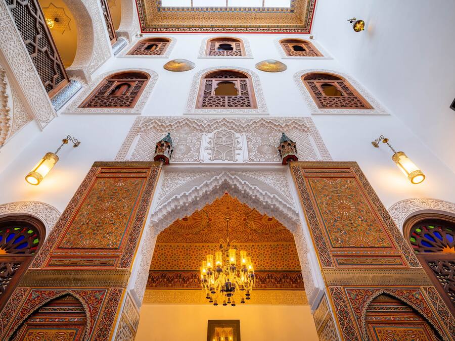 An ornate interior with intricate architectural details, a chandelier, and multiple arched windows.