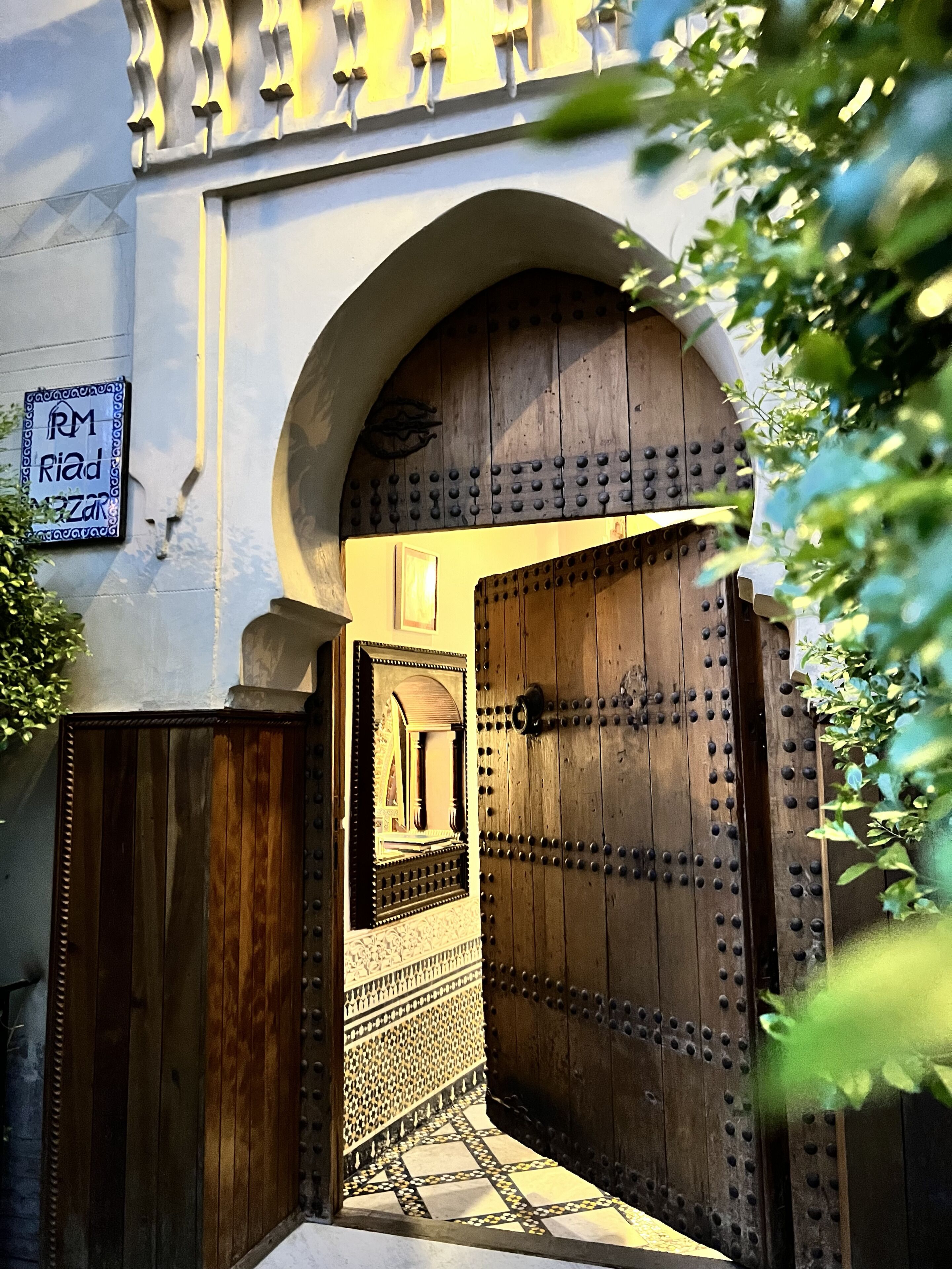 Une porte en bois richement décorée, ornée d’une grille métallique, un hall d’entrée carrelé et une enseigne indiquant la présence d’un restaurant.