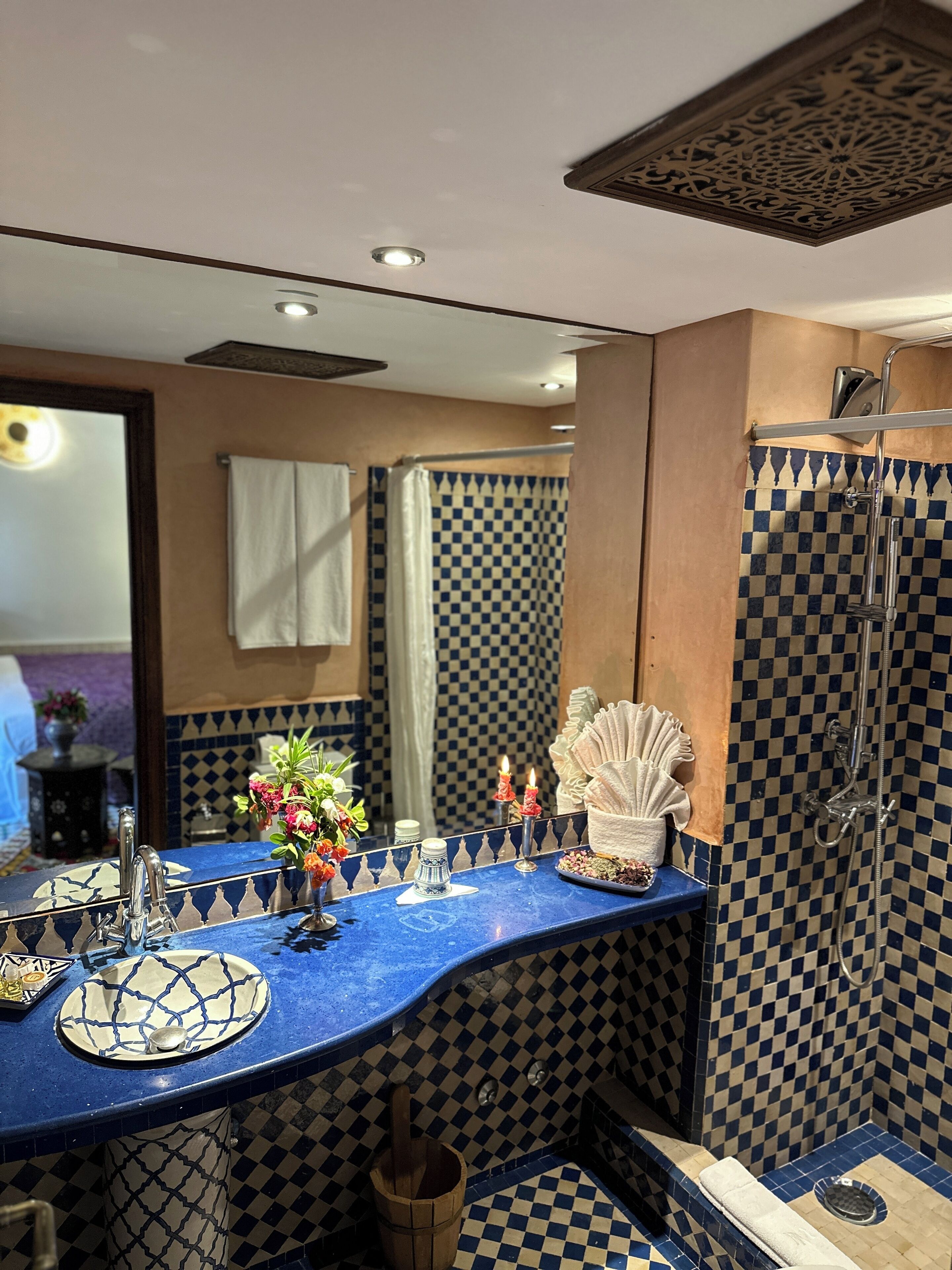 Une salle de bain avec un carrelage à motifs à carreaux, un miroir, un lavabo avec un plan de travail bleu et un espace douche.
