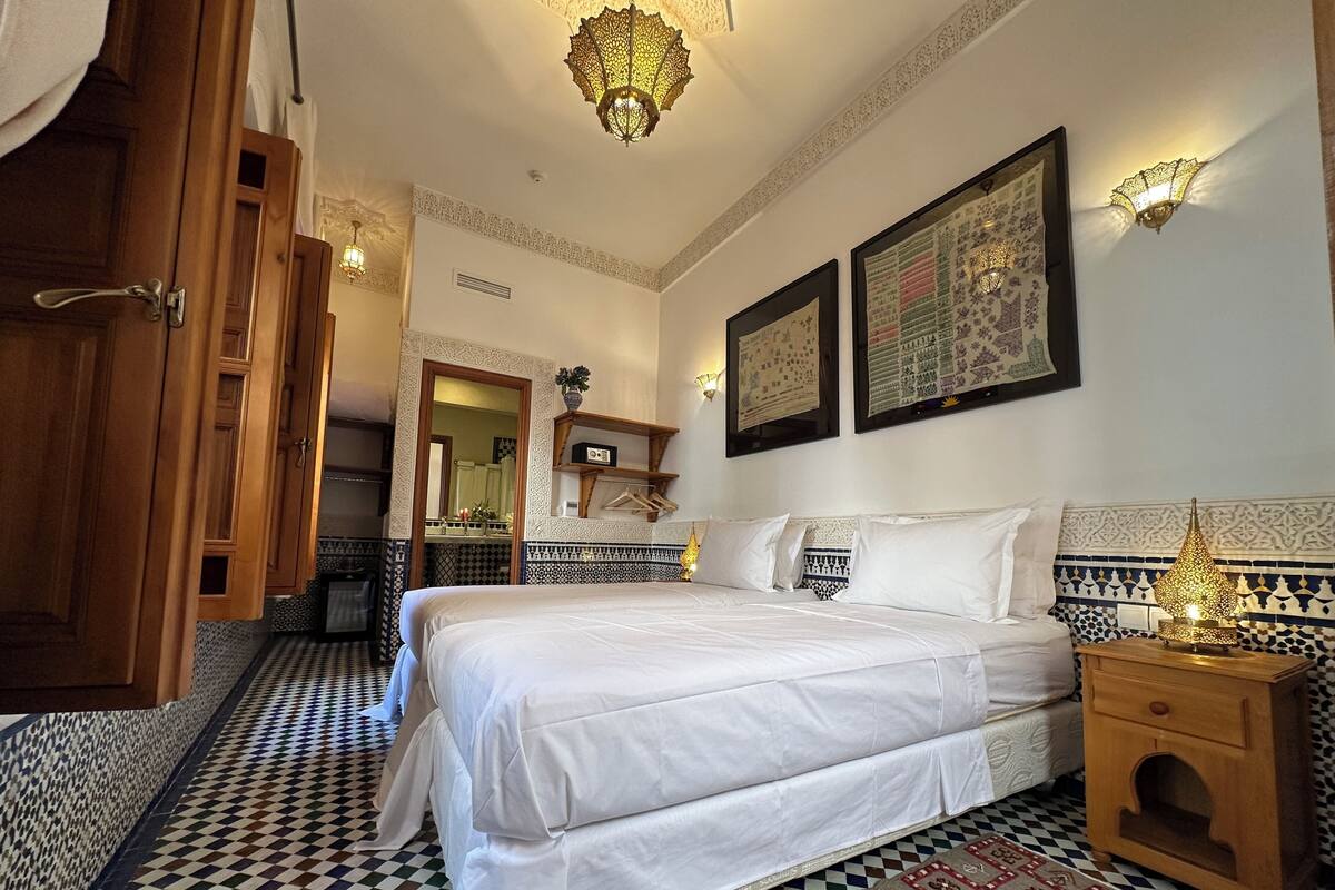 A hotel room with a large bed, a wooden nightstand, a patterned rug, and a decorative wall hanging.