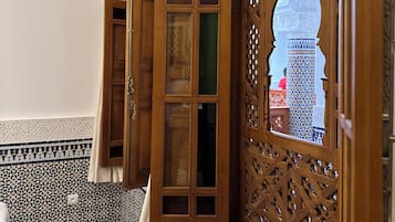A room with intricate tile work, a wooden door with glass panels, and a view of a building through an arched window.