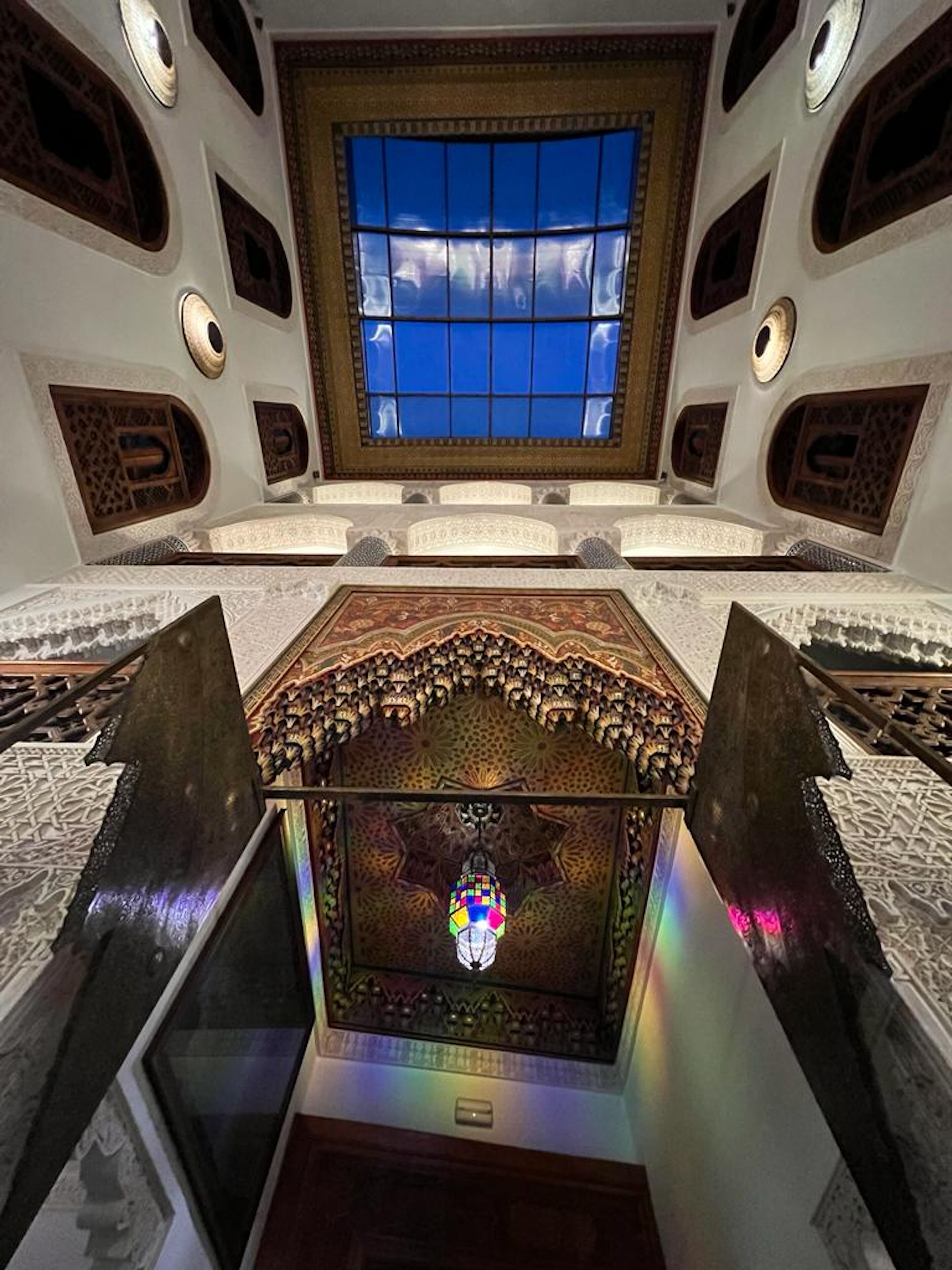 A room with a large window, intricate ceiling patterns, and a central chandelier.