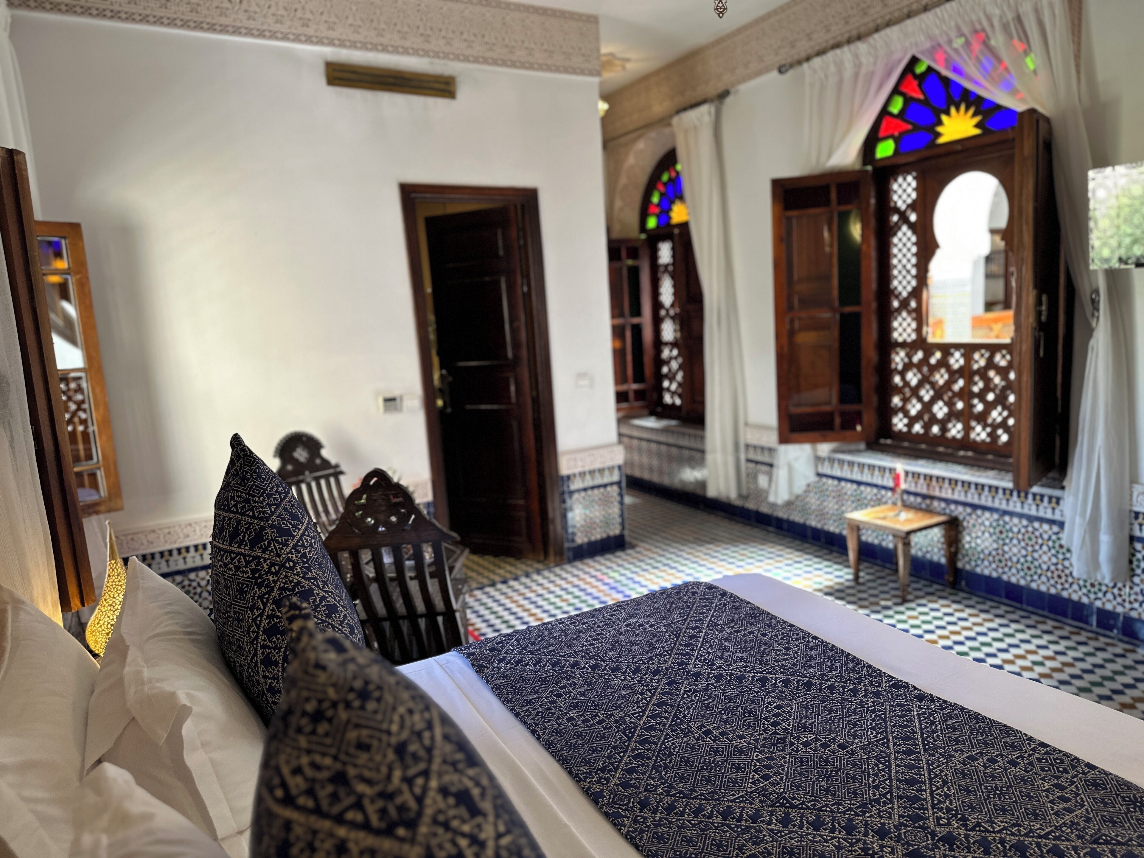 A traditional Moroccan room with a patterned bed, a wooden chair, and a small table.